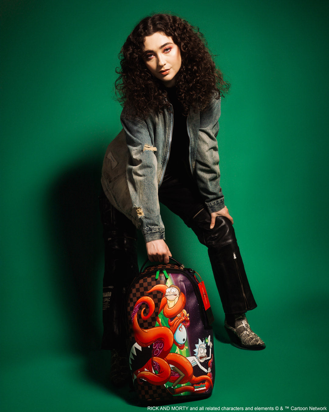 Rick and Morty faux leather backpack standing upright near carry-on luggage