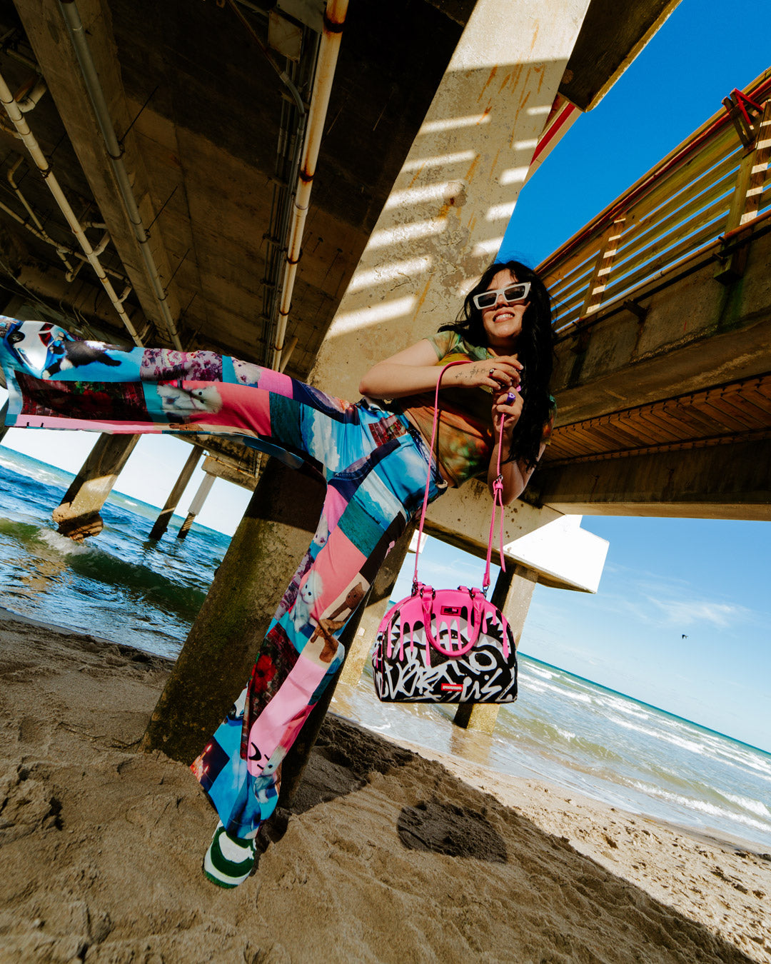 Model wearing the bag crossbody while walking near a beach promenade.