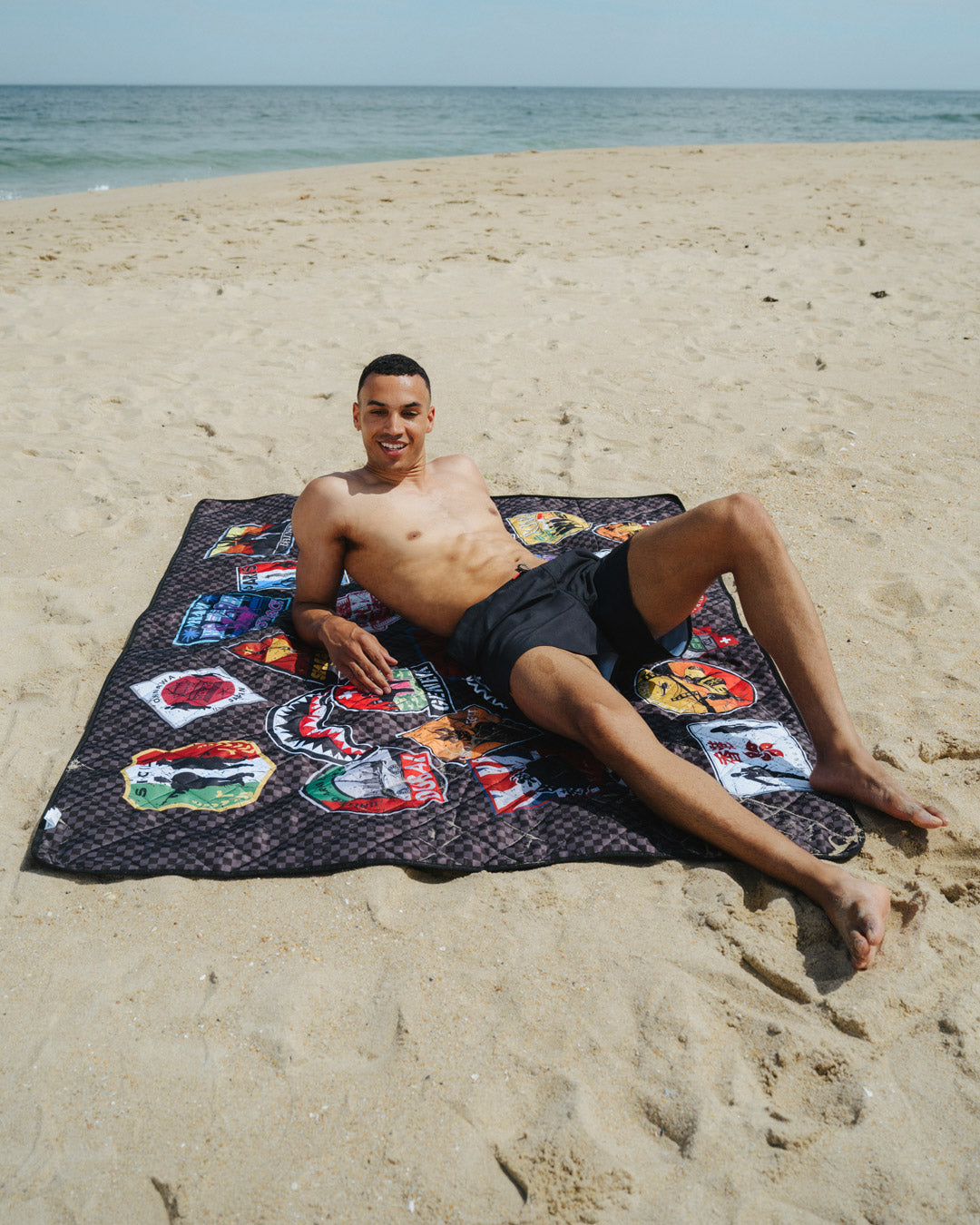 Person lounging on a beach blanket with the tote bag nearby