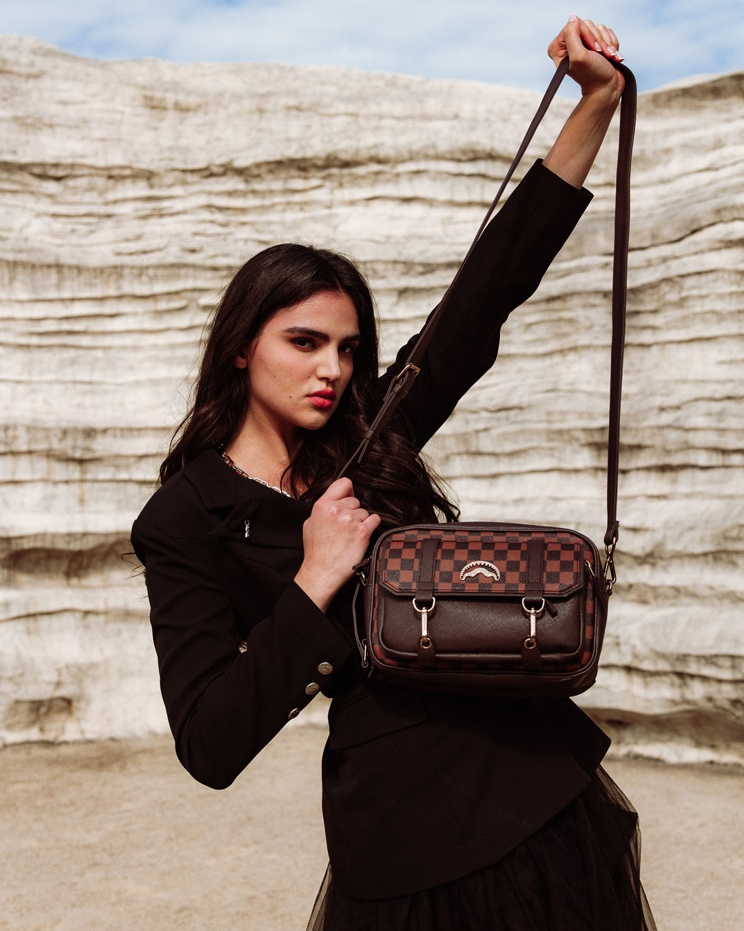 Model wearing leather crossbody bag slung across shoulder in a city park
