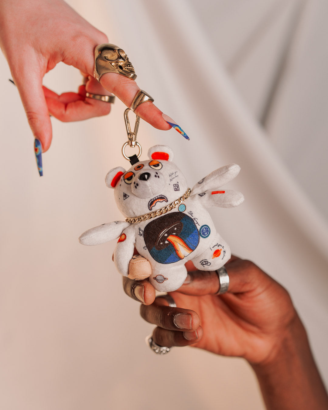 Front view of a soft plush teddy bear keychain with extra arms and gold chain